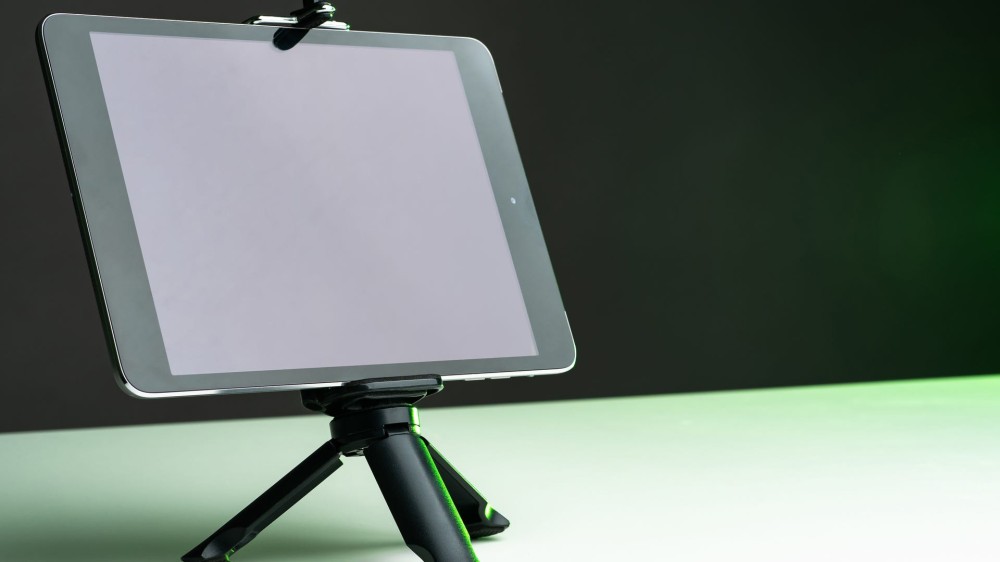 A tablet is mounted on a short tripod that rests on a tabletop.